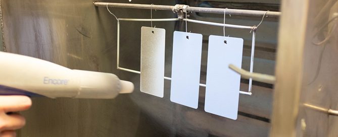 White paint swatches on strings hung from a metal rod, showing various coating and finish options.