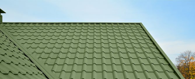 Green corrugated metal roof panels on a residential home with autumn foliage and blue sky.