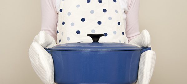 Person in a polka dot apron holding a large blue enameled cookware pot with lid, demonstrating pigment application.