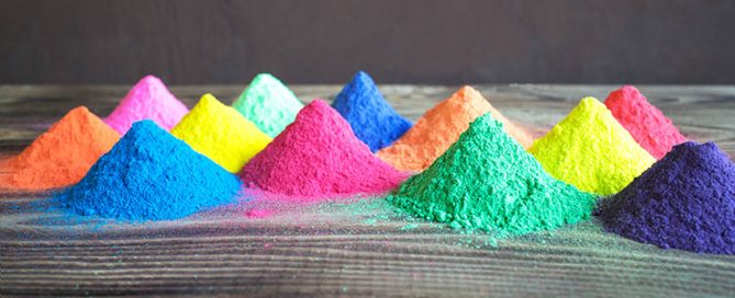 Cone-shaped piles of brightly colored pigment powders on a wooden surface spanning a full color spectrum.