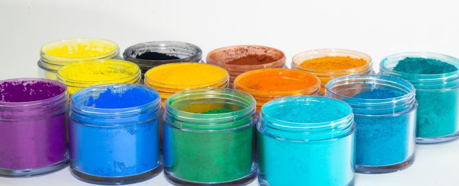 Lab technician in blue wear dispensing magenta pigment powder from a container at a pigment work surface.