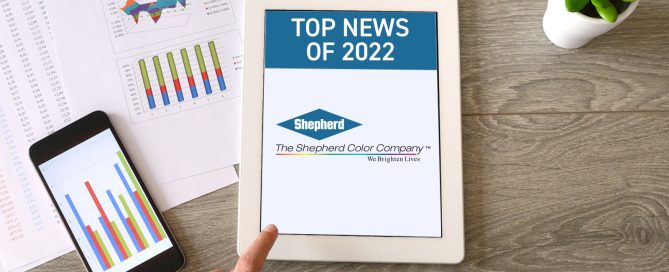 Flat-lay desk scene with a tablet showing Shepherd Color Company's Top News of 2022, surrounded by business charts and a smartphone.