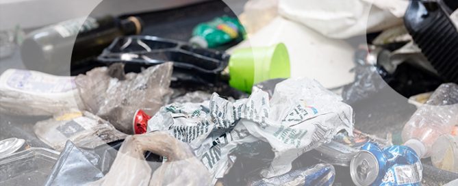 Mixed plastic waste and packaging scattered on a conveyor belt, including films, cones, and bottle caps in a recycling process.